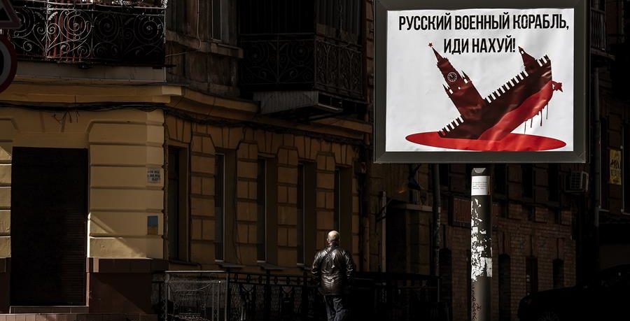 Un ciudadano pasa ante un cartel en el que se puede leer "Barco militar ruso, que os den" y muestra al Kremlin como un barco que se hunde en un mar de sangre en una calle de Odesa.